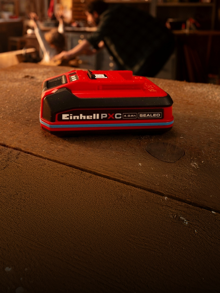 Batteria Einhell Power X‑Change 4.0Ah SEALED su un banco da lavoro in legno, con anello blu e etichetta.