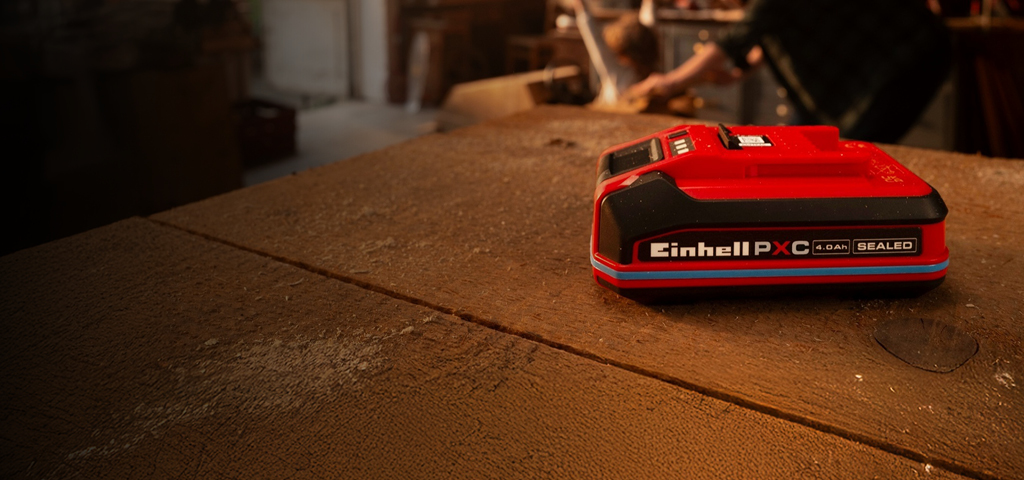 Batteria Einhell Power X‑Change 4.0Ah SEALED su un banco da lavoro in legno, con anello blu e etichetta.