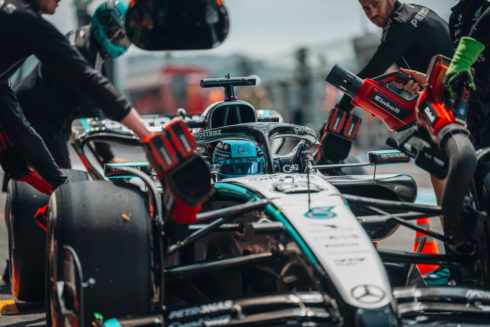 Un’auto del Mercedes-AMG PETRONAS Formula One Team durante un pit stop. I membri del team utilizzano soffiatori senza fili Einhell per raffreddare i componenti del veicolo. La squadra è concentrata e lavora con precisione.