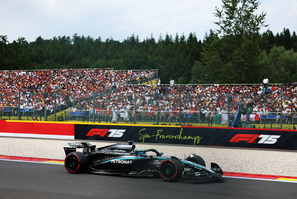 Un’auto del Mercedes-AMG PETRONAS Formula One Team corre sul circuito di Spa-Francorchamps. Sullo sfondo, le tribune gremite sono piene di tifosi che sventolano bandiere internazionali. Il logo di Spa-Francorchamps è visibile sulla barriera.
