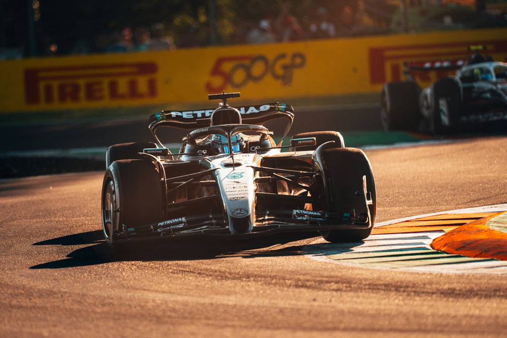 Un’auto del Mercedes-AMG PETRONAS Formula One Team corre su una pista soleggiata durante un Gran Premio. L’auto affronta una curva ad alta velocità con un’altra vettura sullo sfondo.