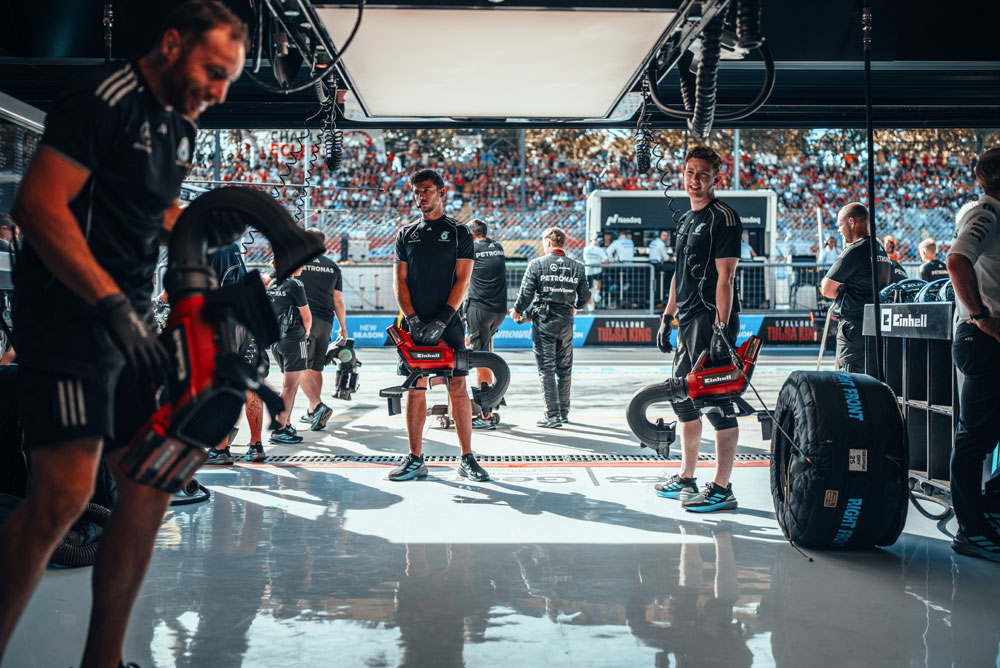 I meccanici del Mercedes-AMG PETRONAS Formula One Team si preparano nel garage con soffiatori senza fili Einhell prima di un pit stop. Sullo sfondo, le tribune sono piene di tifosi.