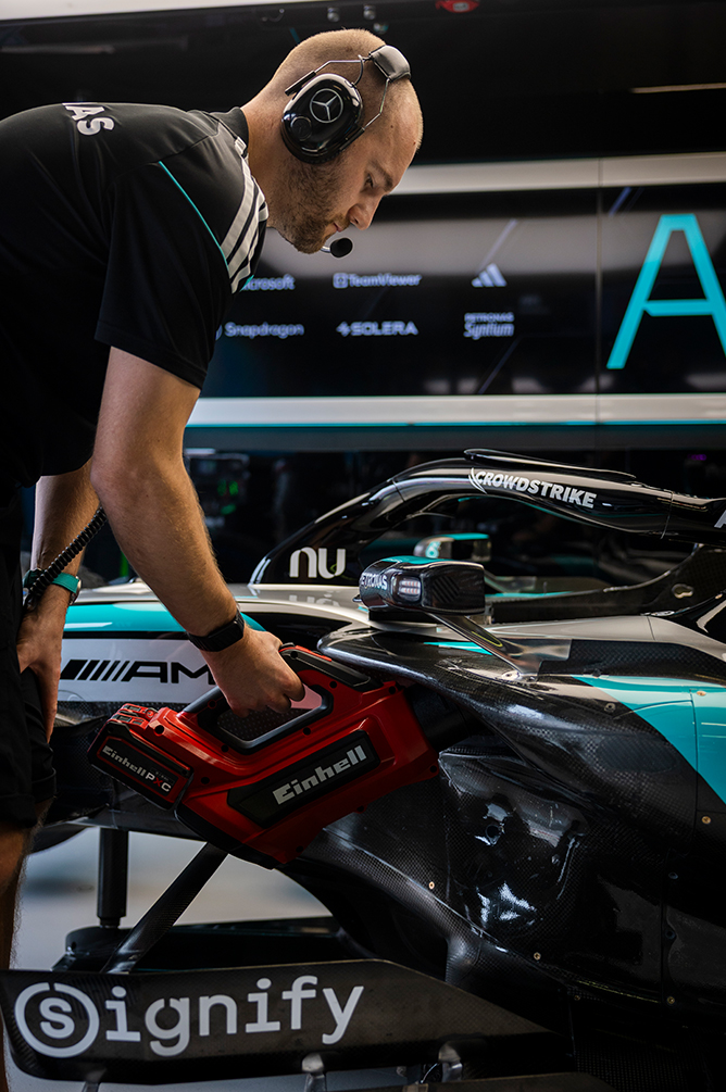 Meccanico di Formula 1 che lavora su una vettura da gara nel garage con un utensile elettrico.