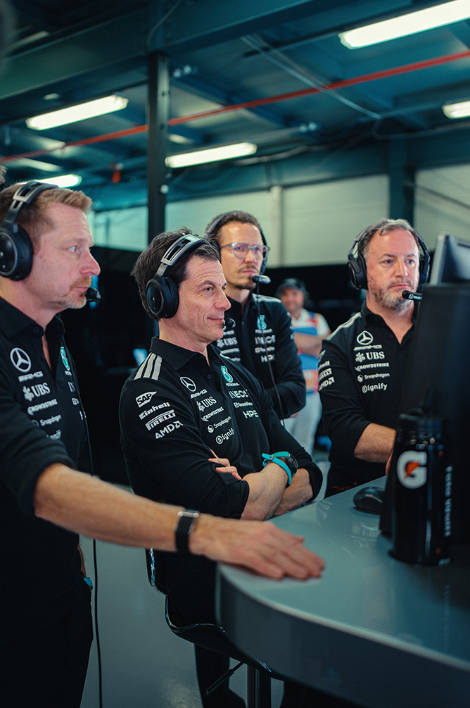 Membri del team di Formula 1 con cuffie che monitorano la gara dal muretto box.