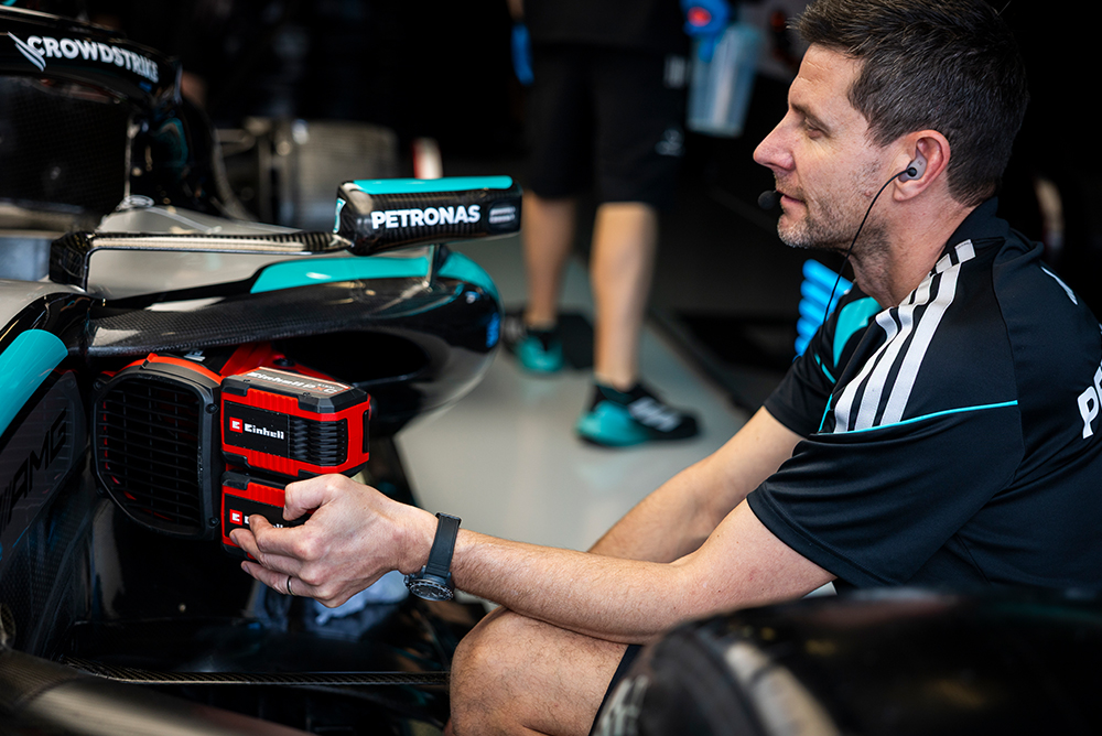 Meccanico di Formula 1 che tiene una batteria Einhell mentre lavora sulla vettura nel garage.