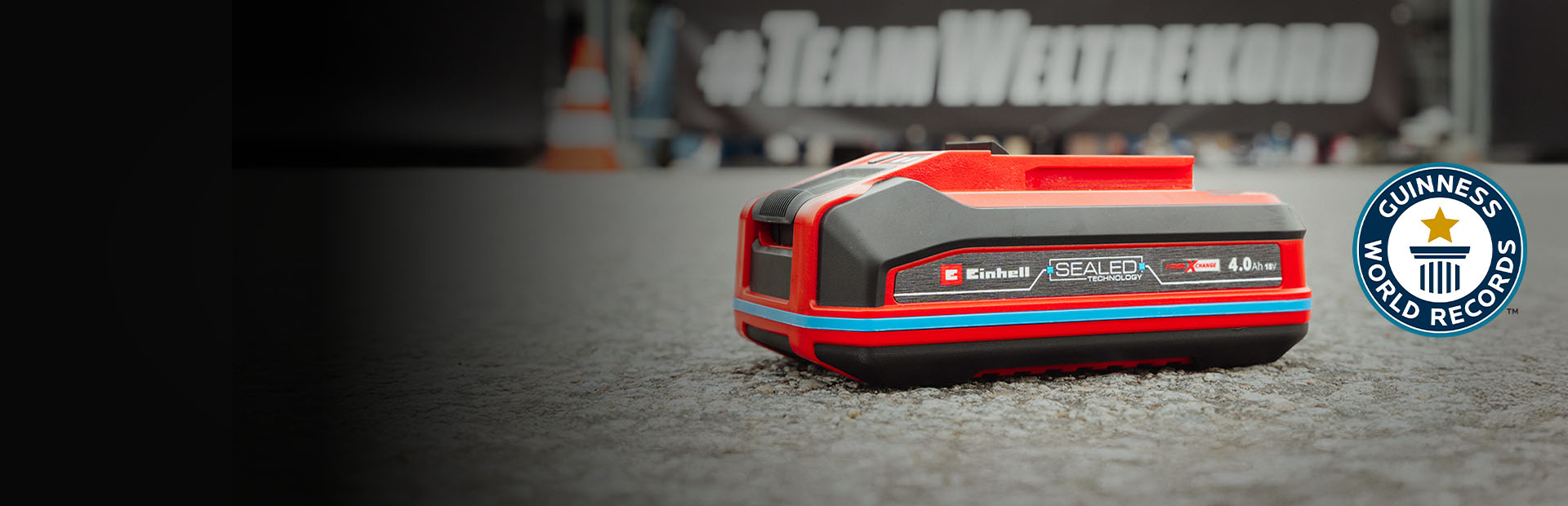 La batteria Einhell SEALED Power X-Change da 4,0 Ah giace sull'asfalto, con il logo “Record Holder” del Guinness World Records sulla destra.