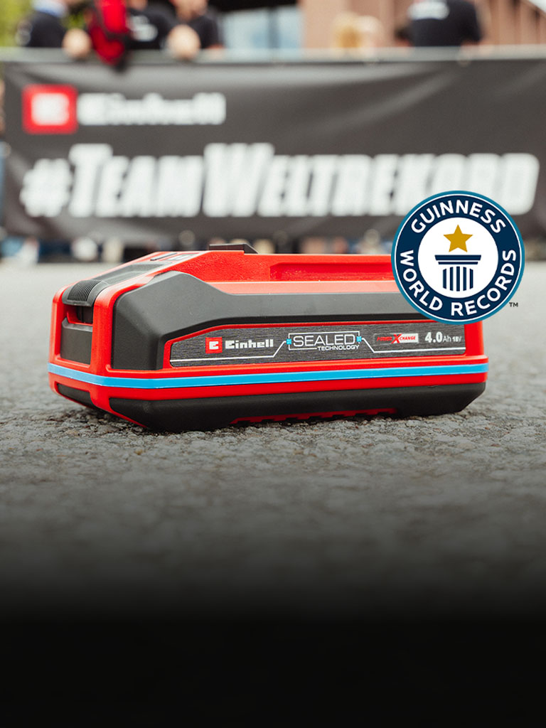 La batteria Einhell SEALED Power X-Change da 4,0 Ah giace sull'asfalto, con il logo “Record Holder” del Guinness World Records sulla destra.