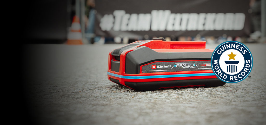 La batteria Einhell SEALED Power X-Change da 4,0 Ah giace sull'asfalto, con il logo “Record Holder” del Guinness World Records sulla destra.