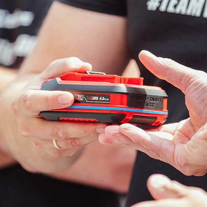 Due persone consegnano una batteria Einhell SEALED Power X-Change 4,0 Ah, mostrata a colori.